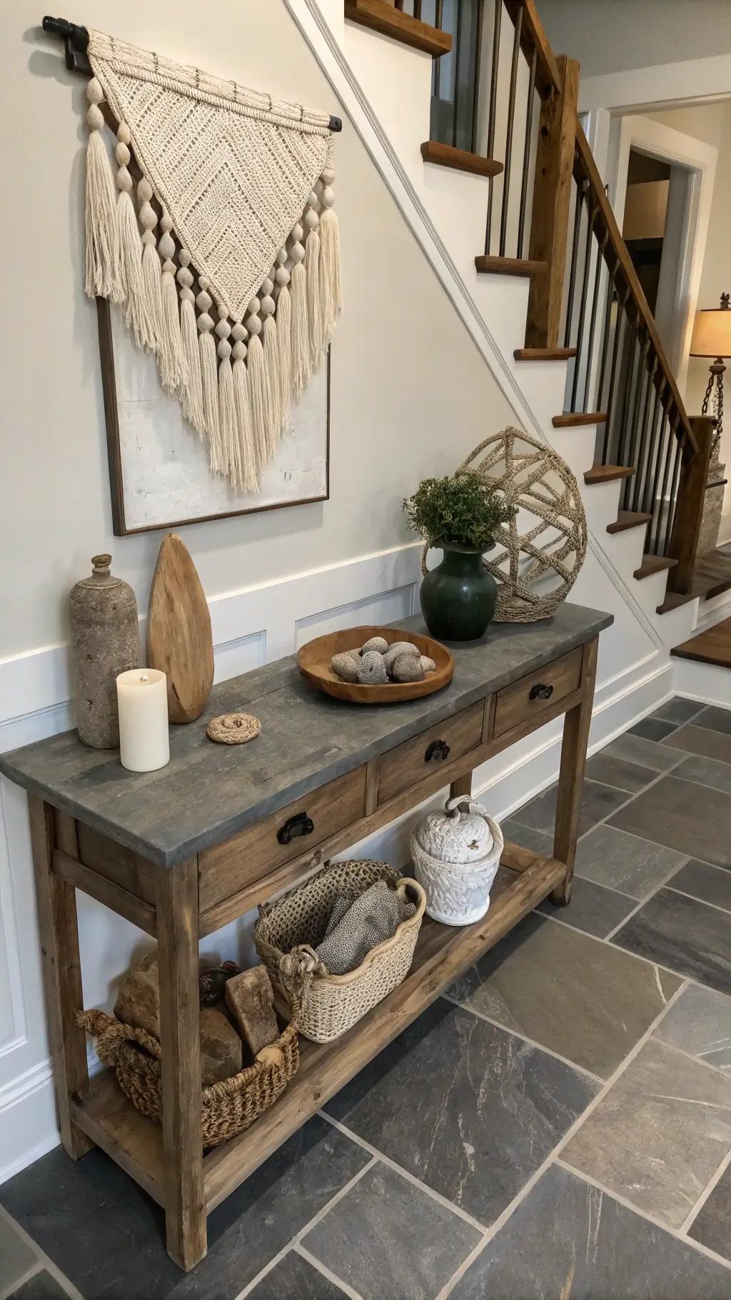 Overhead view of a vintage foyer at twilight, featuring a vintage oak console table with found objects, handwoven wall hanging, and worn limestone flooring with moody lighting.