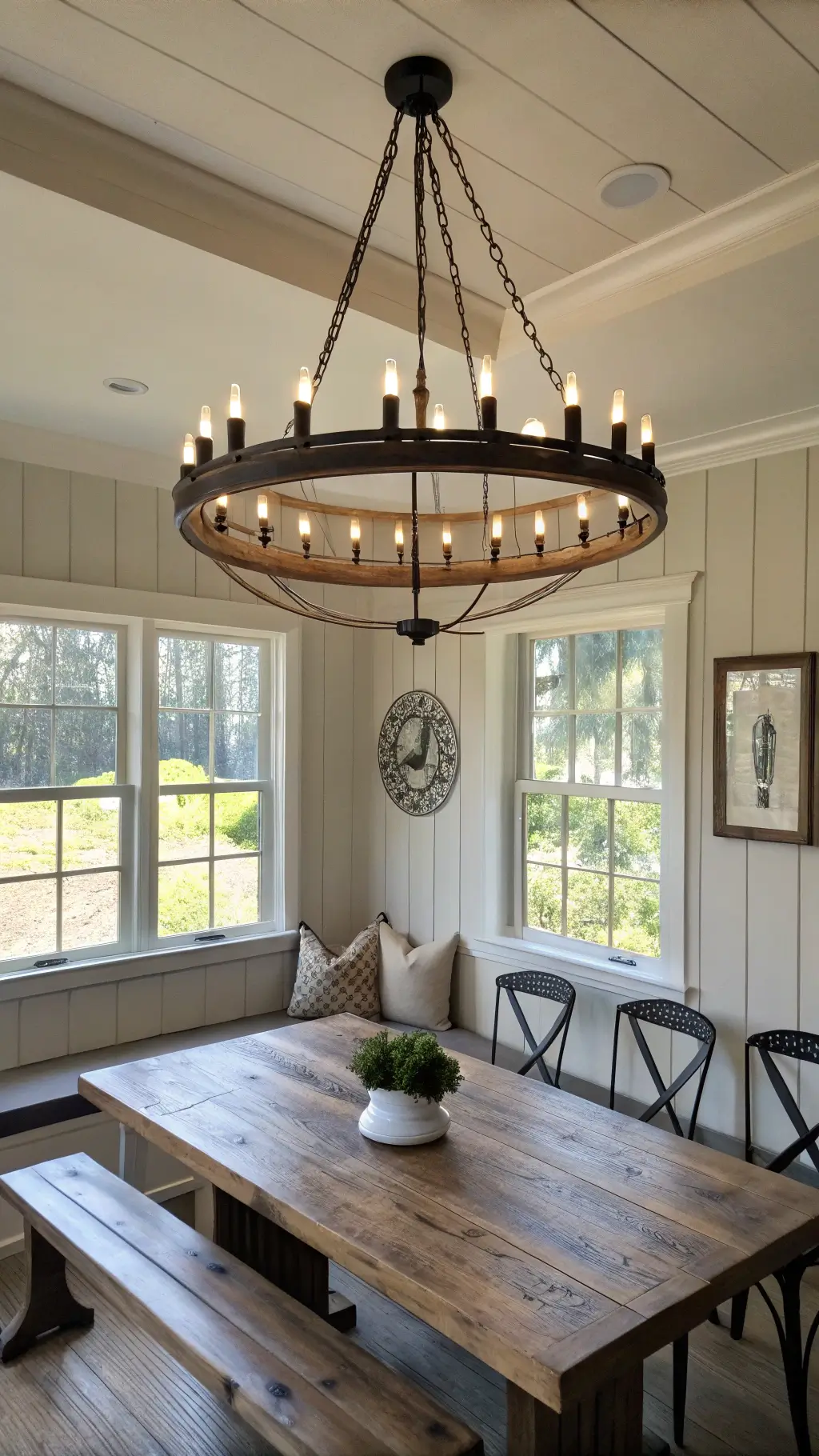 Sun-filled dining area with large iron chandelier, wall-mounted sconces, weathered oak table and vintage decor elements on a neutral color palette.