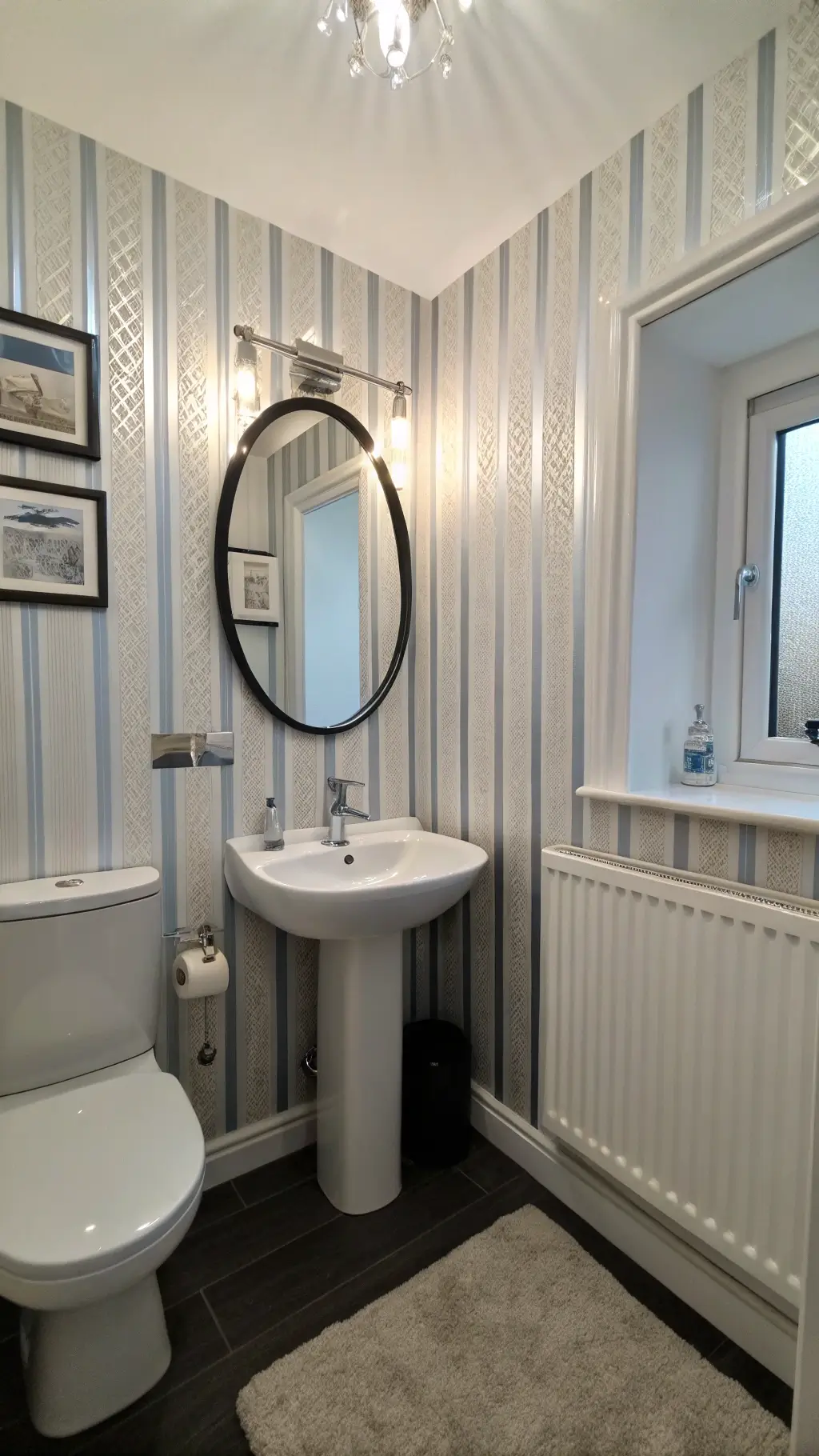 Low-angle shot of a 5x8ft bathroom with vertical striped wallpaper, full-wall mirror reflecting a freestanding sink and wall-mounted tapware, under a powder blue ceiling illuminated by cool morning light.