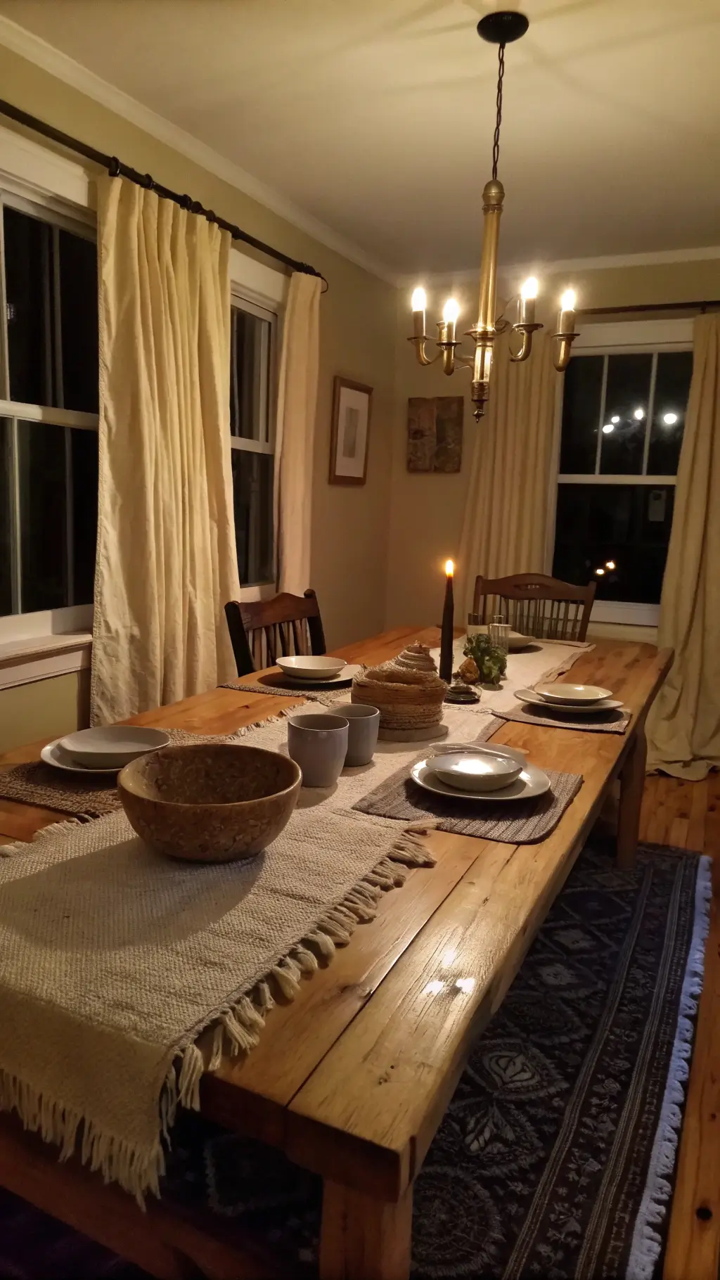 Warmly lit dining room with raw silk curtains, an ancient maple table with a handwoven wool runner, stone bowls and handmade cups on the table, shot at table height.