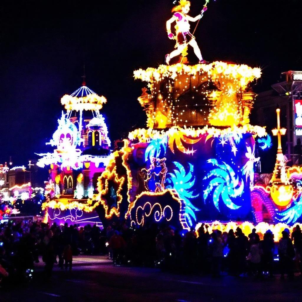 Illuminated floats with intricate light designs at the Starlight Parade during nighttime, reflecting vibrant colors off street lights creating a magical atmosphere